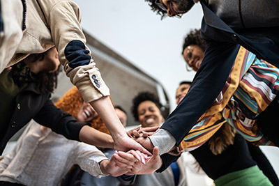 What We Offer people gathered in a circle with hands stacked in the center