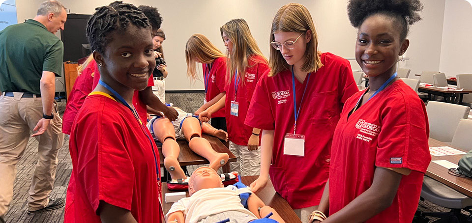 Students standing around a practice doll in a classroom