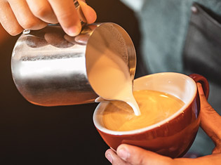 Close up view of a hand pouring coffee creamer into a red cup