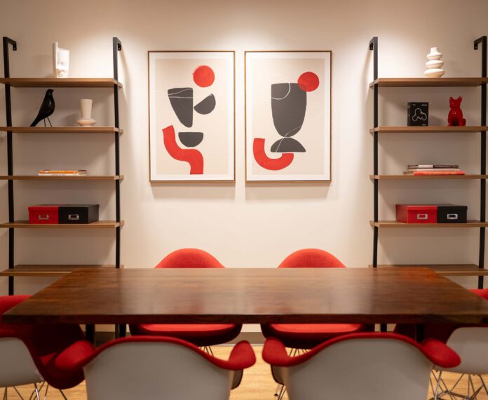 Decorative room with red, white, black and gray colors on bookshelves, art on wall and table and chairs.