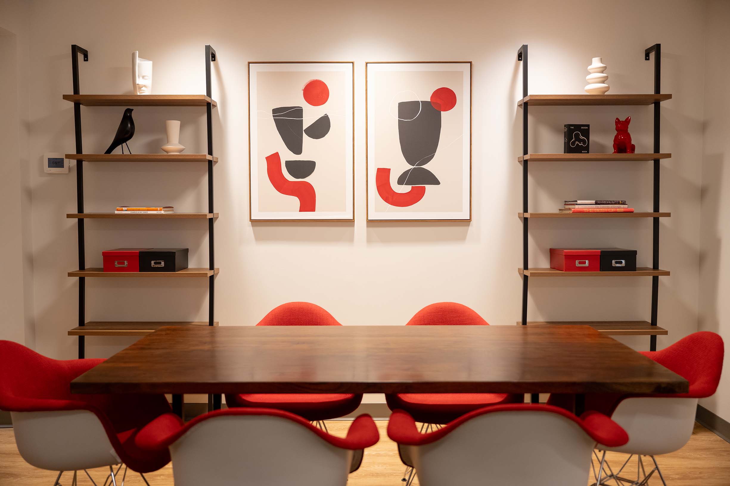 Decorative room with red, white, black and gray colors on bookshelves, art on wall and table and chairs.