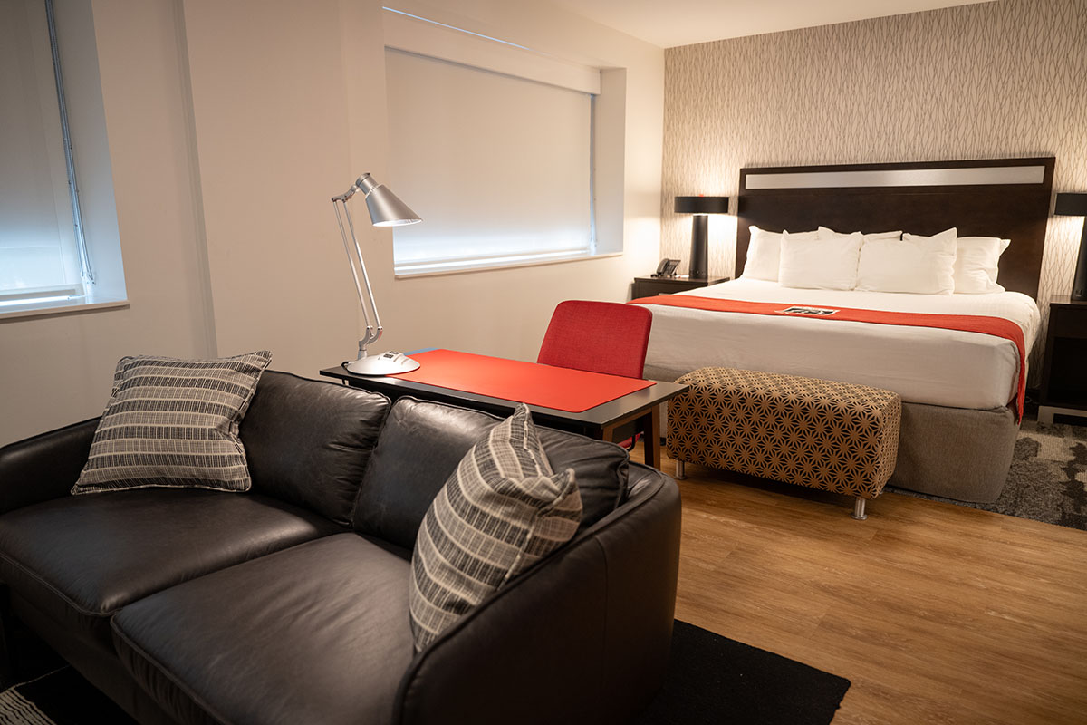 View of a suite at the Georgia Center with a couch in the foreground, desk and chair, and a bed in the background.
