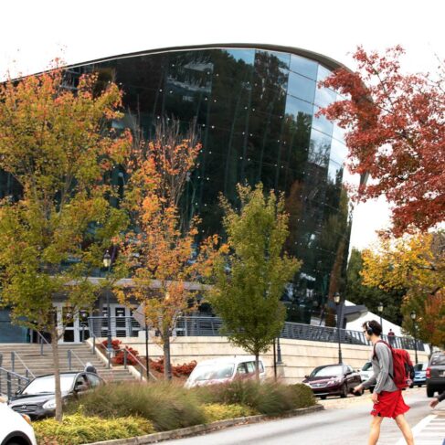 Exterior of Stegeman Coliseum with fall foliage and students on the street and sidewalks in the foreground