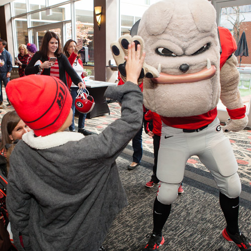 Hairy Dawg, wearing football outfit, giving a high five to a child wearing a red hat and gray coat