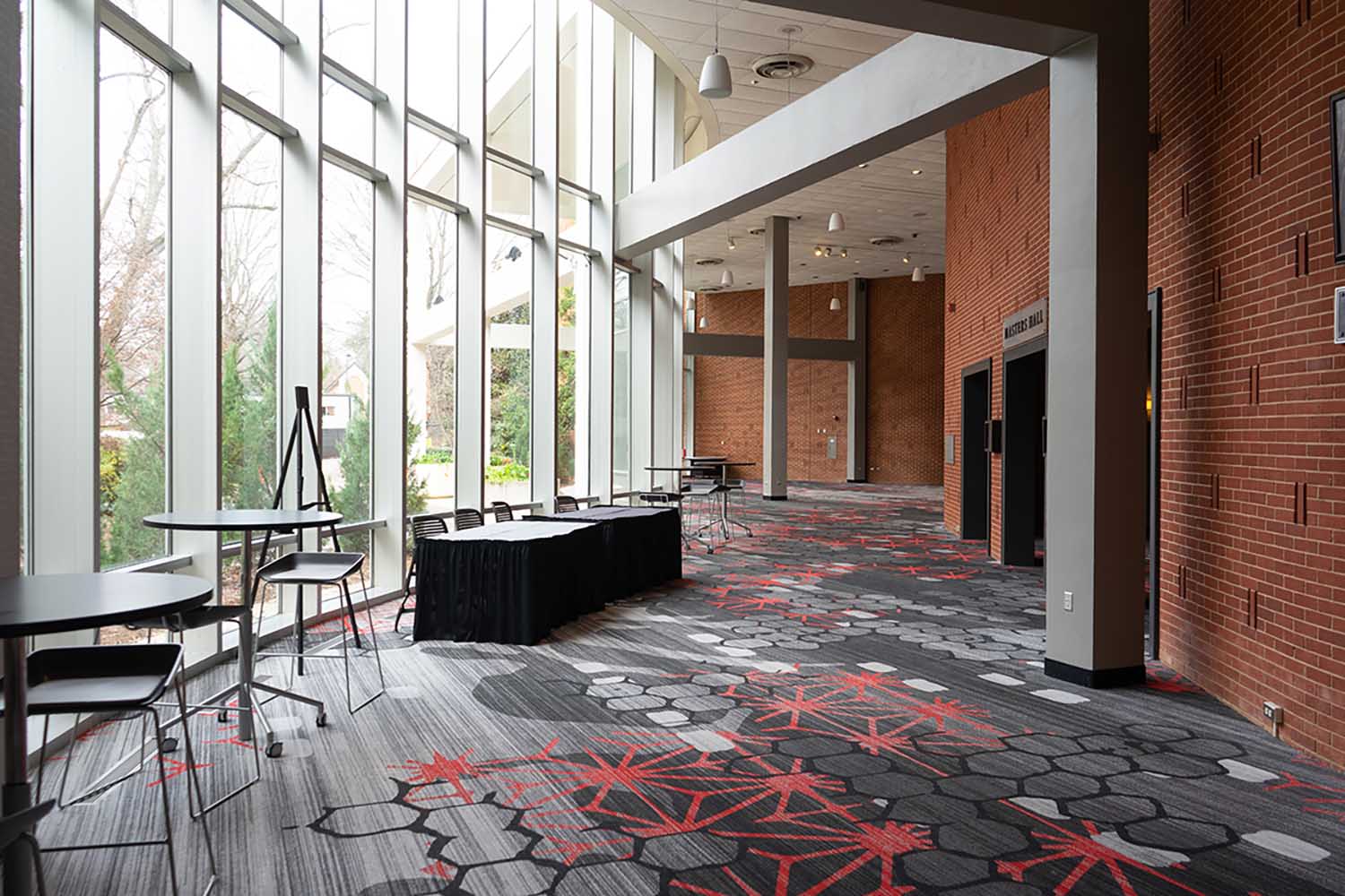 View of the Hill Atrium with floor to ceiling windows on the left and tables and chairs along the windows.