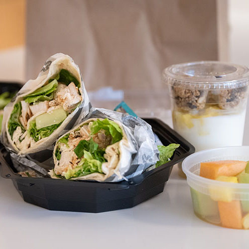 View of a wrap, salad, cut fruit, and drink in to go containers.