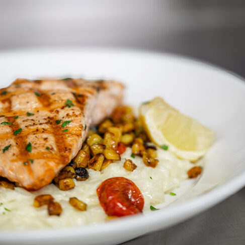 Close up view of salmon, corn, rice, tomato, and lemon on a white place
