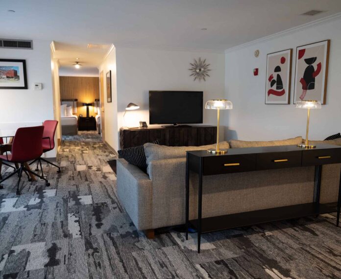 Alumni Queen Suite viewing the living area with TV, console, couch, tables, and chairs.
