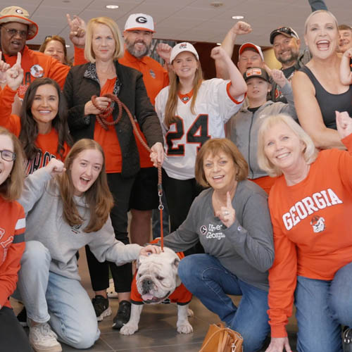 Georgia fans posing and cheering beside UGA bulldog mascot.