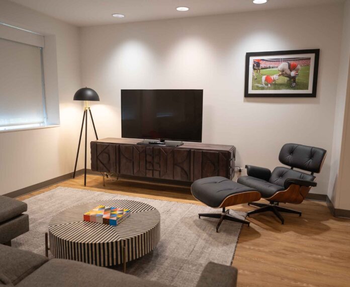 President's King suite with a lamp, TV on a console, black lounge chair, and a black and white stripe coffee table
