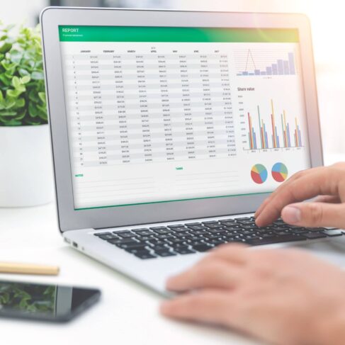 A laptop screen displaying a spreadsheet with report graph on a desk.