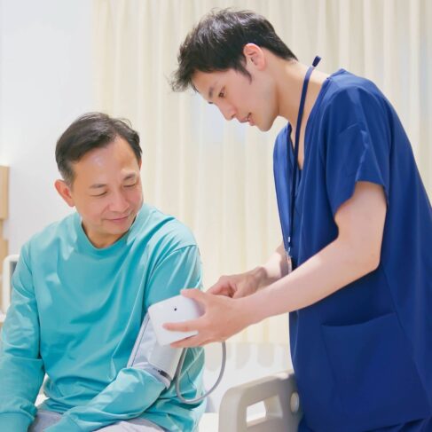 A male nurse is measuring blood pressure of senior man in hospital ward