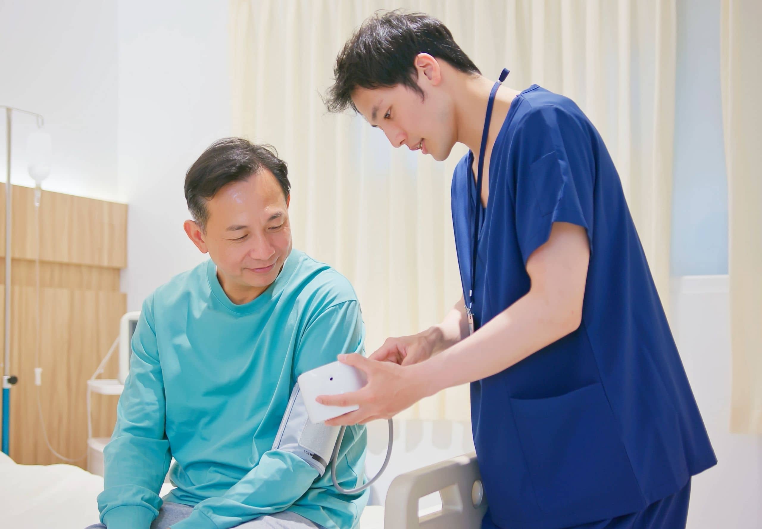A male nurse is measuring blood pressure of senior man in hospital ward
