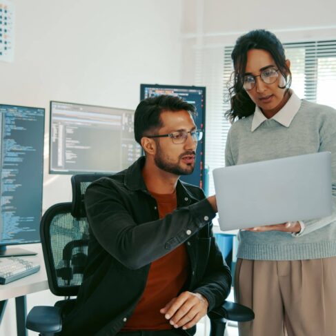 Two programmers reviewing code on a laptop in a modern office