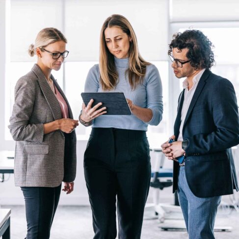 A female manager holding a tablet device showing her co-workers their project plan.
