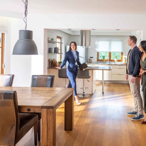Young female real estate agent showing couple modern kitchen and dining room in apartment