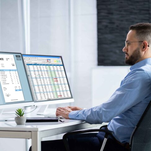 A person working with a digital electronic billing system and an invoice on his monitors.