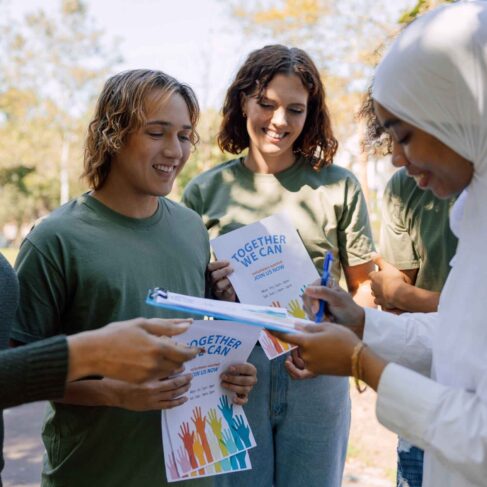 A group of volunteers encouraging people to give to their cause/foundation as they hold up sign up sheets and posters