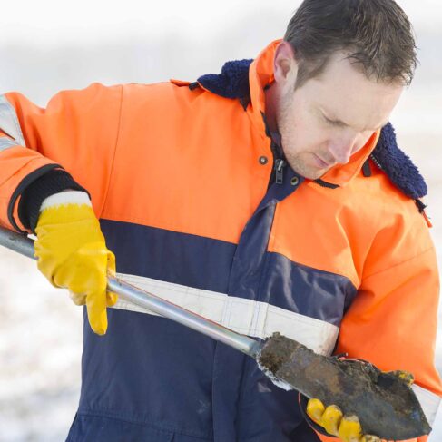A worker wearing a orange and navy jacket, conducting a soil test.