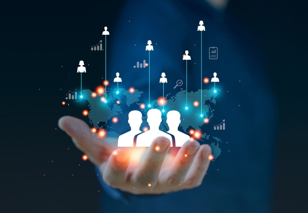 A hand holds a digital representation of people icons connected to various data points and graphs, symbolizing networking, data analysis, or human resources management.