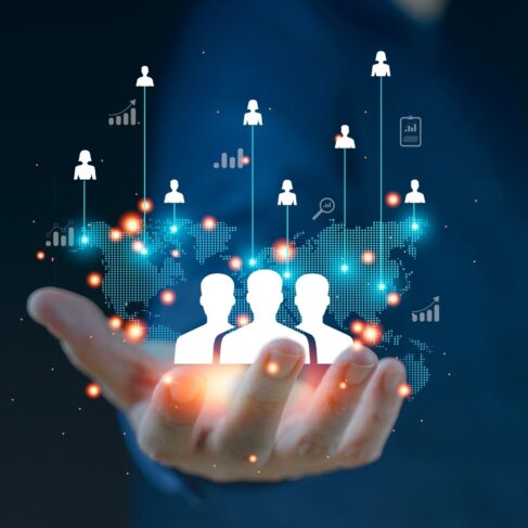 A hand holds a digital representation of people icons connected to various data points and graphs, symbolizing networking, data analysis, or human resources management.