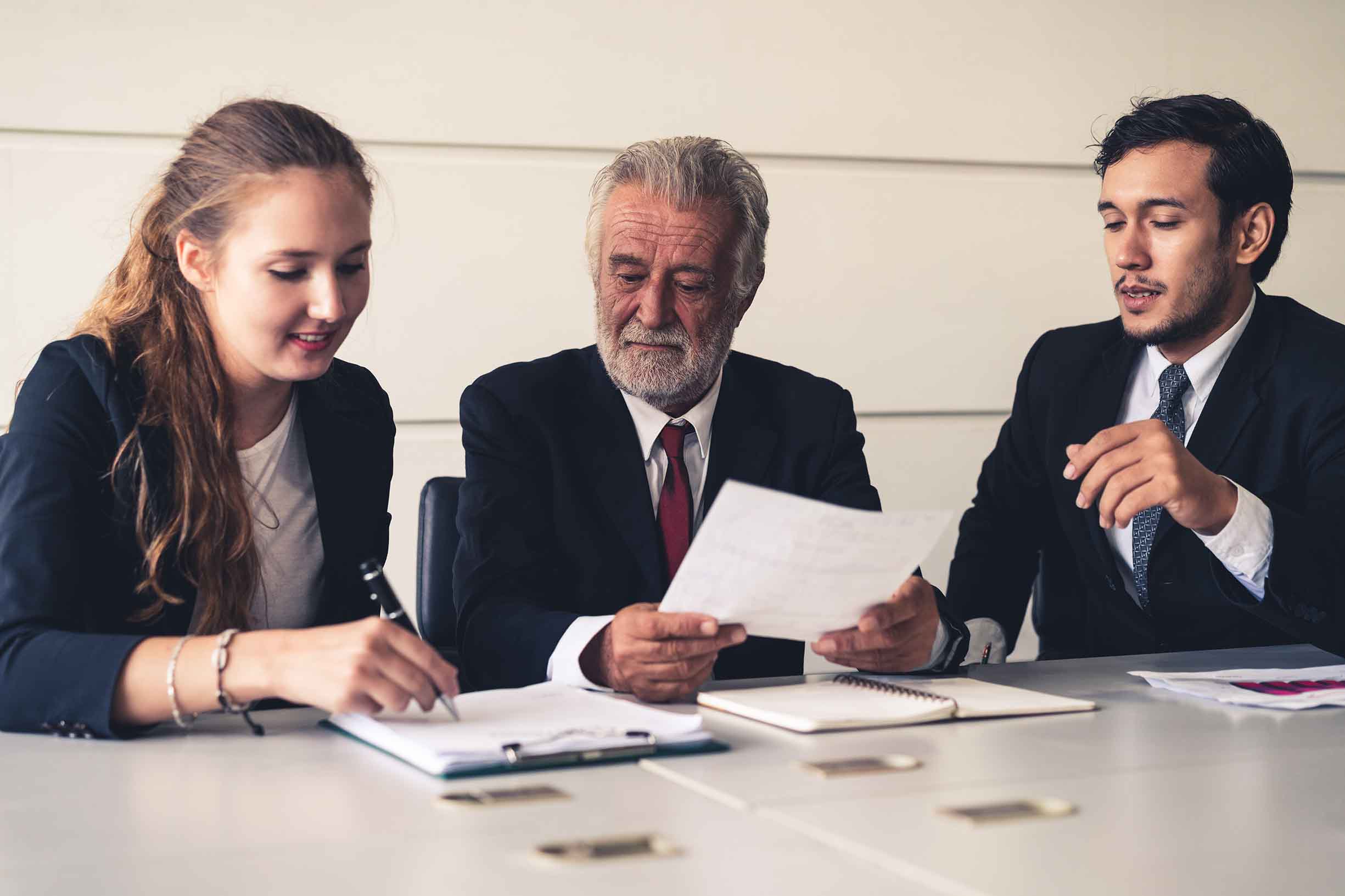 Senior old executive manager working with young businesspeople in office meeting room. Old man is the company leader sitting with secretary and translator. International corporate business concept.