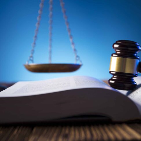 The gavel, scales of justice, books, wooden table are displayed on a table with a blue background