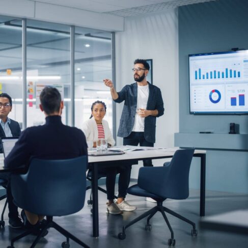 Businessman Leads Business Meeting with Managers, Talks, uses Presentation TV with Statistics, Infographics. Digital Entrepreneurs Work on e-Commerce Project.
