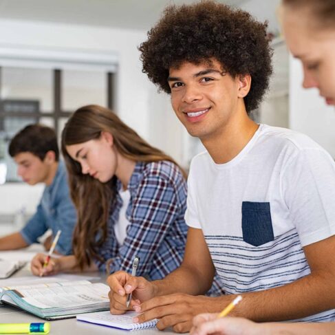 Portrait of smiling student looking at camera with classmates sitting near him. Group of college students taking active part in lesson while sitting in lecture hall.