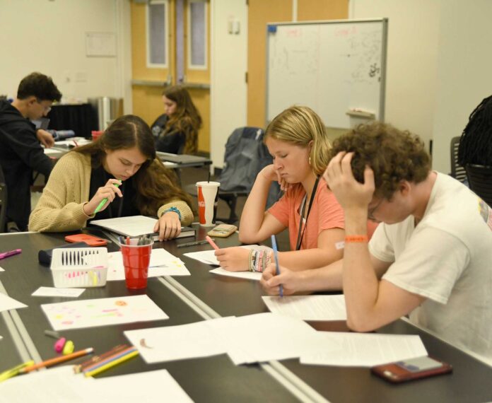 three students sitting at a table writing on paper