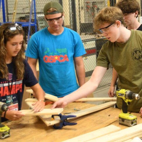 Four students working a project using lumber and electric drills.