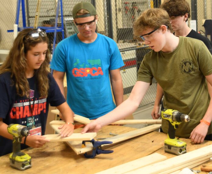 Four students working a project using lumber and electric drills.
