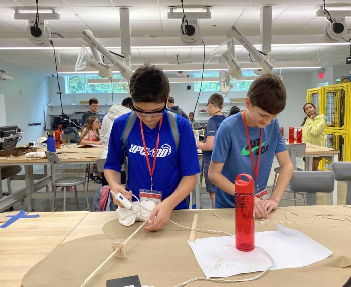 Two students working on a engineering project in a classroom with many students.