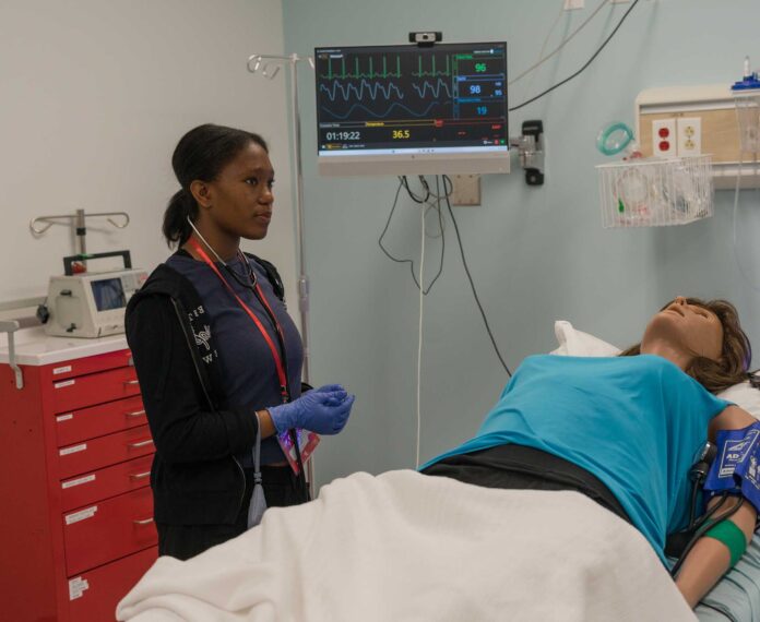 A medical student stands by the gurney of her practice model