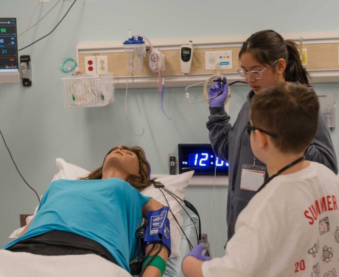 Students hold stethoscope and practice drills on a test patient