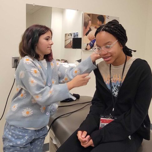 Student looking into another student's ear with medical device.