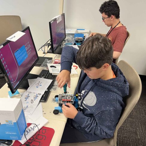 Student holding a screwdriver building a robot in front of a computer