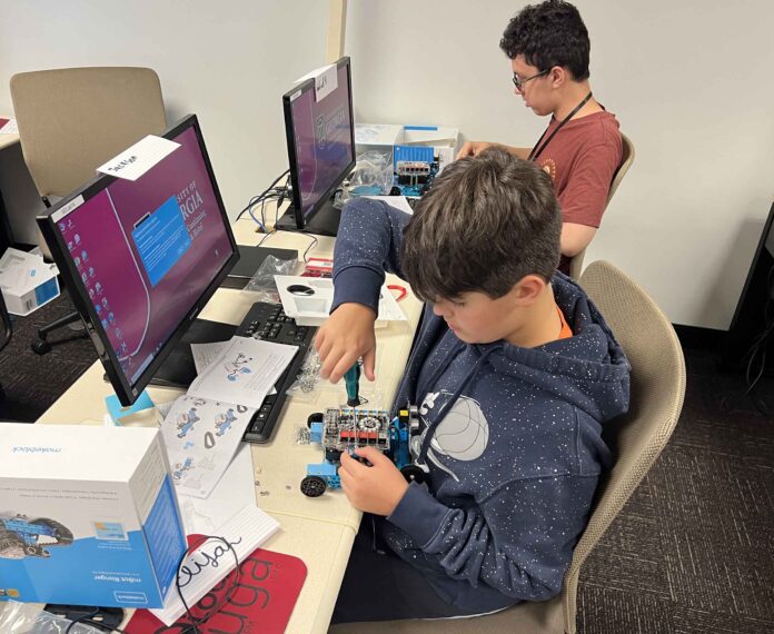 Student holding a screwdriver building a robot in front of a computer