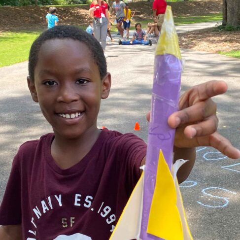 Student holding a small purple and yellow rocket outside