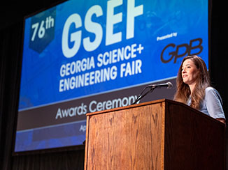 Laura Brewer standing at a wooden podium at the Georgia Science and Engineering Fair event.
