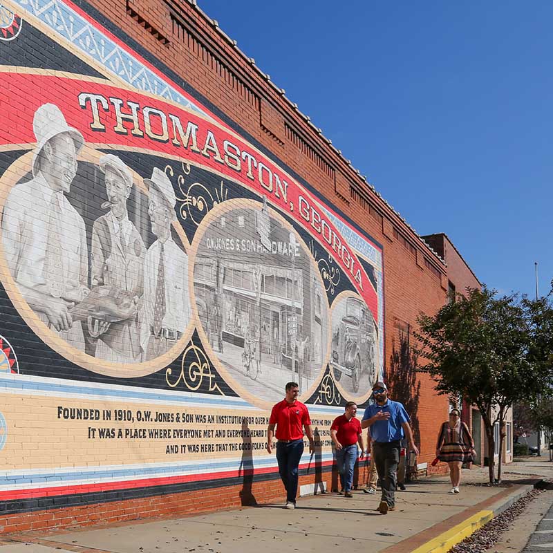 People walking in front a a brick building with a painted image of Thomaston, Georgia history.