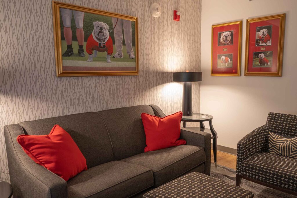 View of the UGA Famous Suite looking at bulldog pictures on the wall and couch with red pillows