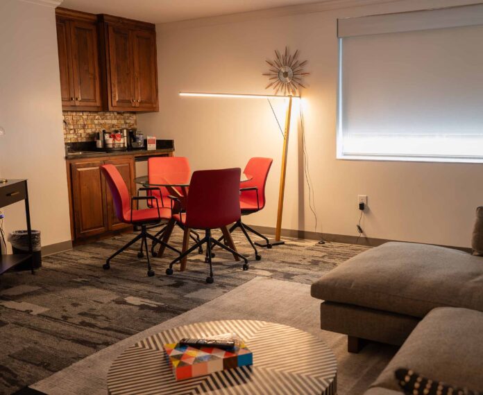 View of the Vice Presidents Queen suite with cabinets, table and chairs, floor lamp, stripe coffee table and couch in the foreground.