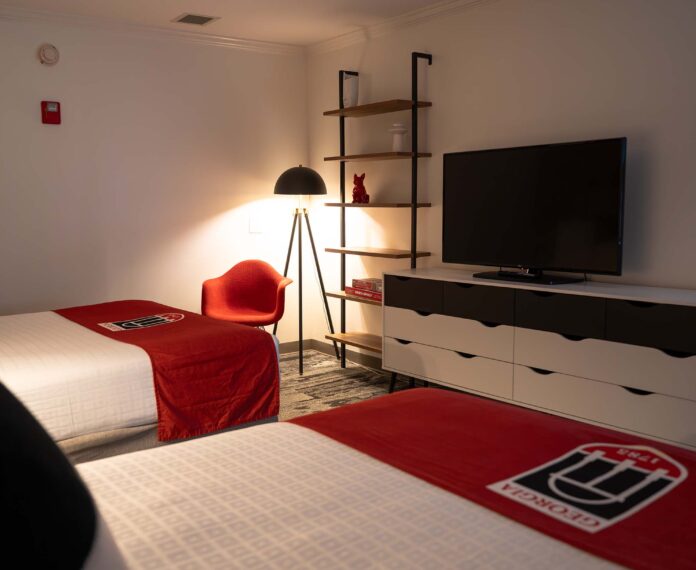 View of the Vice Presidents Queen suite with floor lamp, shelves, TV on a console with two beds in the foreground