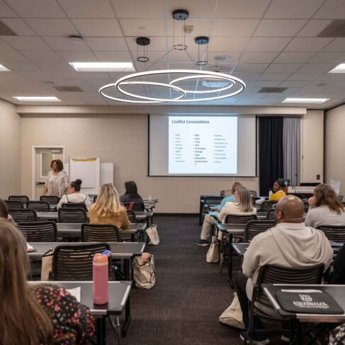 a group of people sitting in a classroom looking at a PowerPoint presentation