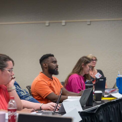 Students sitting at a table with computers and papers in front of them.