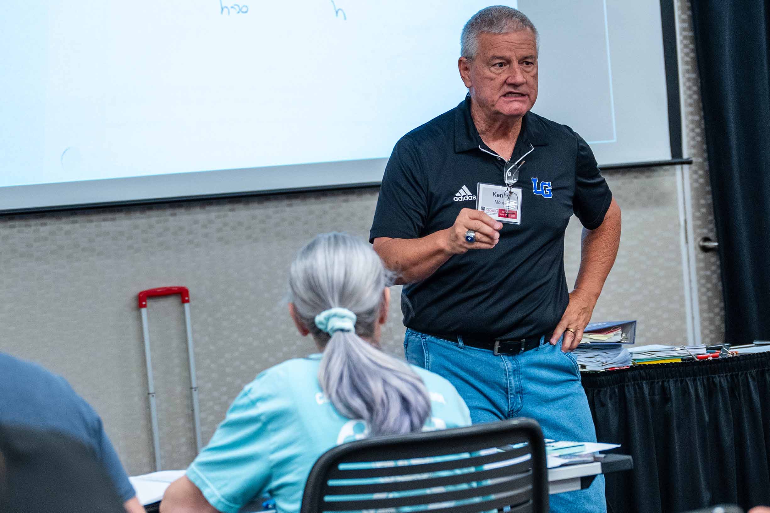 Instructor Kevin standing in front a screen, teaching in a classroom with a female student in front of him.