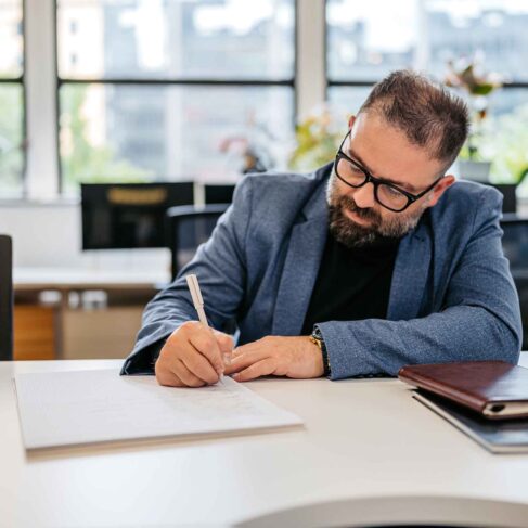 Handsome mid-adult man writing in a notebook at the desk in the office building.