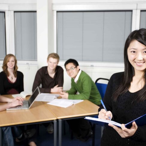 Five students studying in a lecture room. Girl writing in pad in foreground