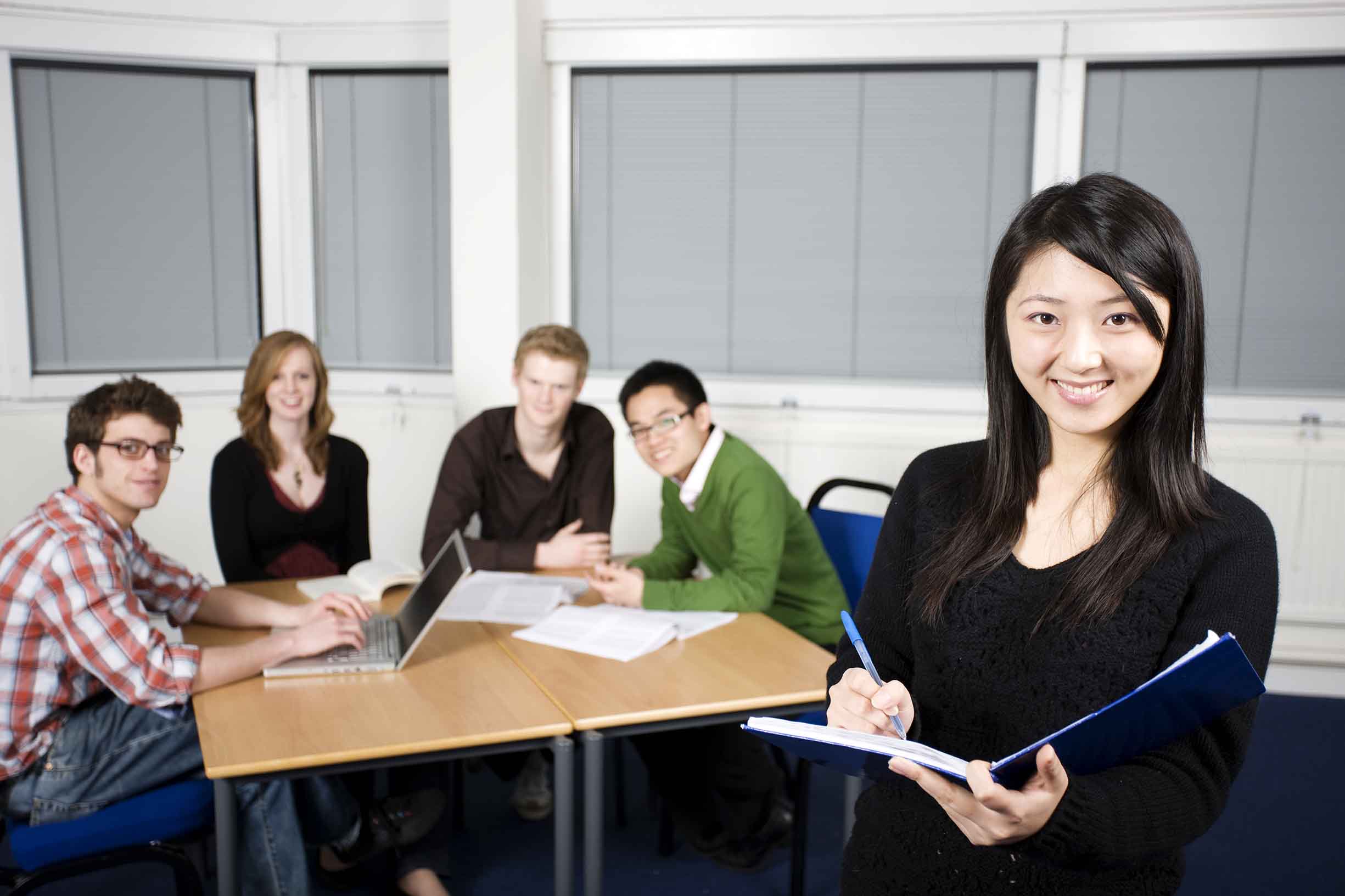 Five students studying in a lecture room. Girl writing in pad in foreground